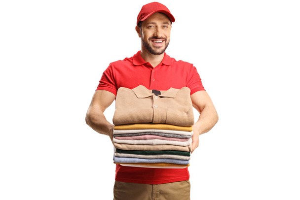 Male worker holding a pile of folded clothes and smiling isolated on a white background - Photo, image