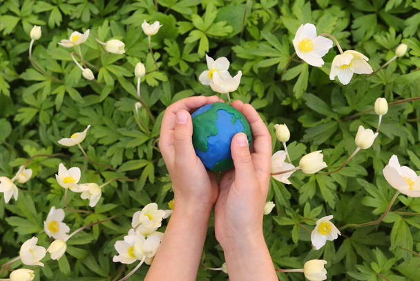 enfant tient une planète en plasticine Terre sur un fond de fleurs. Concept jour terre, sauver l'environnement. - Photo, image