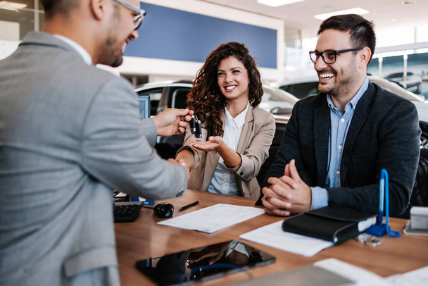 Middle age couple choosing and buying car at car showroom. Car salesman helps them to make right decision. Man signs buyers contract. - Φωτογραφία, εικόνα