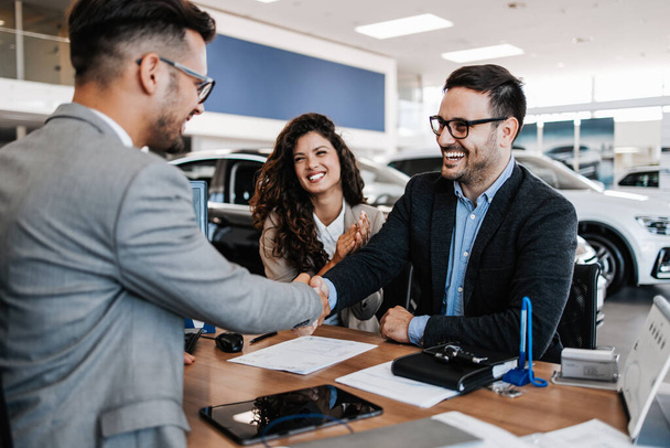 Middle age couple choosing and buying car at car showroom. Car salesman helps them to make right decision. Man signs buyers contract. - 写真・画像