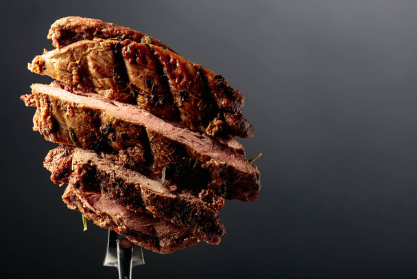 Grilled ribeye beef steak on a black background. Beef steak on a fork.  Copy space. - Photo, Image