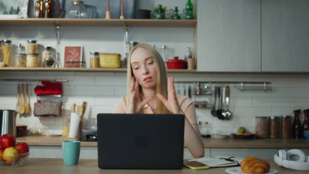 Tired online manager consulting webcam remotely sitting kitchen with modern laptop. Attractive blond woman talking on web camera having video meeting. Serious girl freelancer working in internet. - Photo, Image