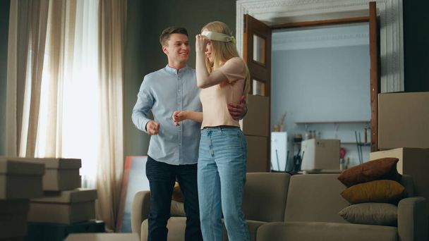 Successful young man buy apartment to attractive blond wife making surprise. Happy woman removing bandage hugging husband rejoicing moving in new house. Cheerful guy showing keys from modern flat. - Foto, Imagem