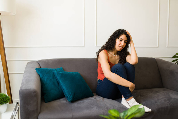 Osamělá mladá žena pocit smutku a deprese, zatímco trpí úzkostí sedí na pohovce doma - Fotografie, Obrázek