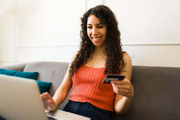 Opgewonden mooie jonge vrouw lachen en plezier hebben tijdens het betalen voor haar online winkelen met een creditcard - Foto, afbeelding