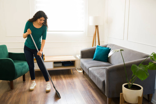 Mexická mladá žena zametat podlahu obývacího pokoje a dělat domácí práce nebo úklid domácí práce u ní doma - Fotografie, Obrázek