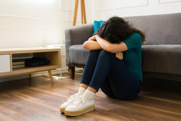 Masentunut nuori nainen yksin olohuoneessa halaamalla polviaan kärsii masennuksesta ja mielenterveysongelmista - Valokuva, kuva