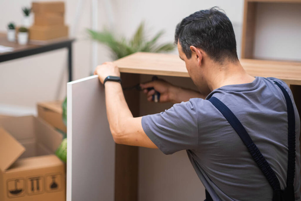 Nábytek montáž v domě zákazníka zkušený muž upevnění bílých dveří na dřevěné skříně specialista na profesionální uniformu pracuje s vlastní prefabrikovaný nábytek - Fotografie, Obrázek