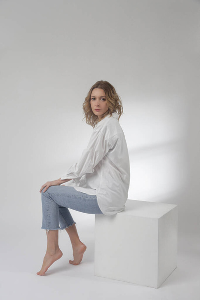 Fashion portrait of young woman in white cotton button down shirt and blue jeans on the white background - Fotó, kép