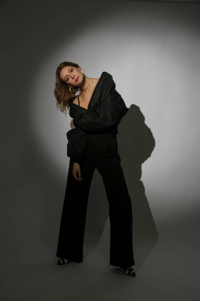 Fashion portrait of beautiful female model wearing black bomber jacket and trousers under spotlight. Female beauty, fashion and glamour concept. - Fotó, kép