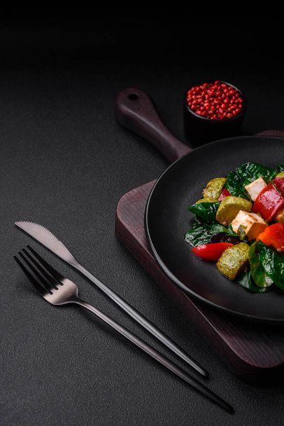 Delicious fresh salad of zucchini, cheese, sweet peppers, spinach with spices and herbs in a ceramic plate on a dark concrete background - Foto, afbeelding