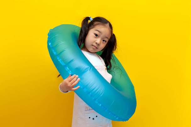 niña asiática con anillo de natación inflable sobre fondo aislado amarillo, el concepto de viajar al mar en verano, niño coreano se va de vacaciones - Foto, imagen