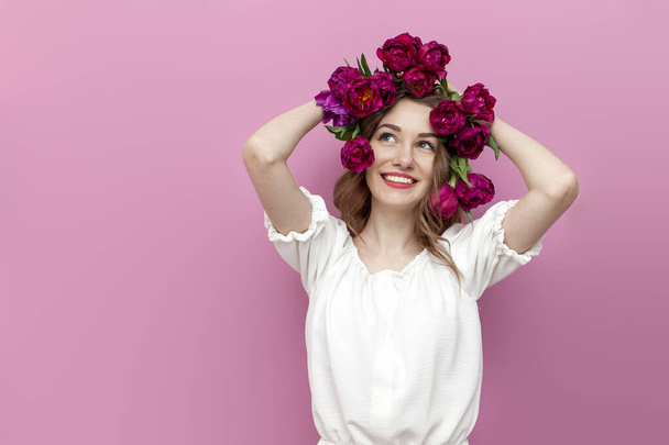jovem menina concurso com tulipas rosa em seu cabelo pensa e sonha com fundo isolado rosa, mulher com flores na cabeça olha para o espaço de cópia, conceito de cuidado do cabelo, conceito de primavera - Foto, Imagem