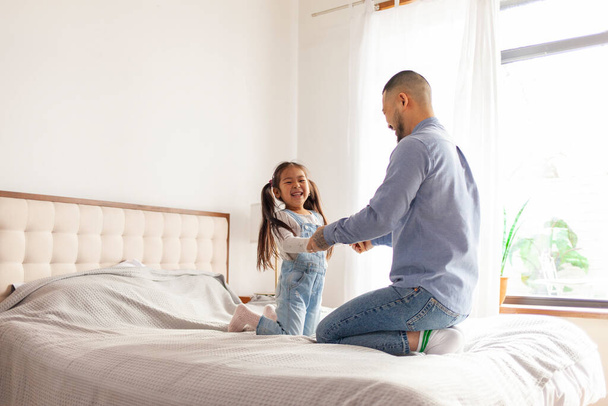 little asian girl jumping on bed at home with dad, korean man playing with daughter, young happy family, dad love concept - Photo, Image