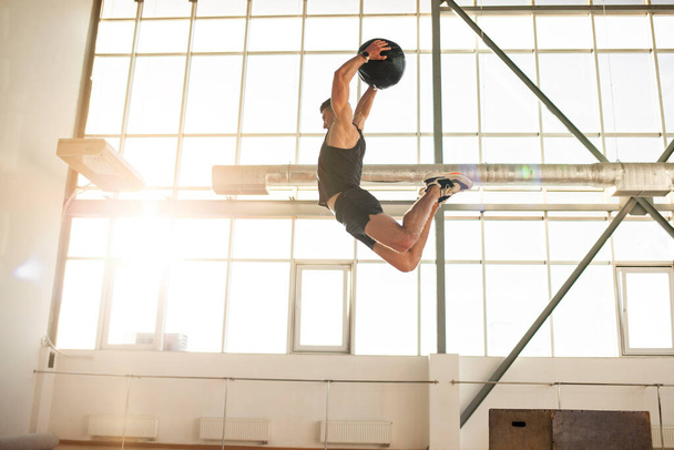 спортсмен на тренировках прыгает и бросает медицинский мяч в тренажерный зал, сильный человек делает фитнес с мячом и делает спортивные упражнения в прыжке - Фото, изображение