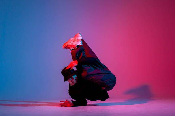 jonge man danser in zwarte kleren breken dansen in neon verlichting, man voert hip hop beweging in rood blauw club verlichting - Foto, afbeelding