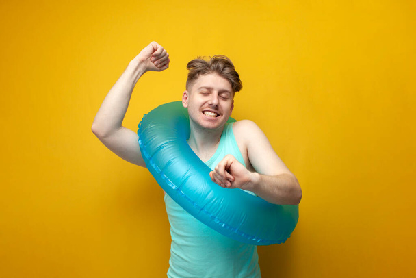 jonge man in de zomer op vakantie met een opblaasbare zwemcirkel verheugt zich en danst op een gele achtergrond - Foto, afbeelding