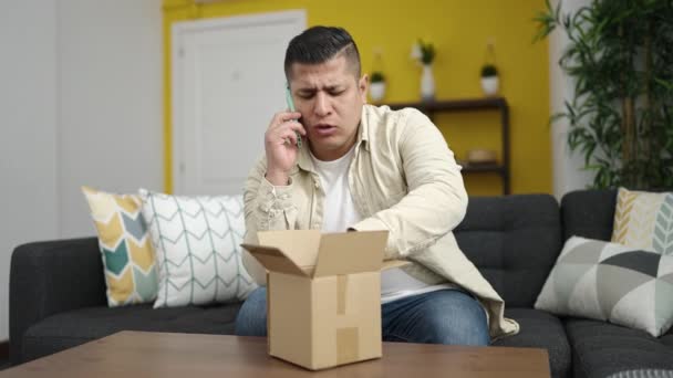Jovem hispânico falando no telefone desembalando caixa de papelão em casa - Filmagem, Vídeo