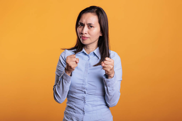 Aggressive filipino fighter doing self defense gesture in studio standing over yellow background. Defensive woman clenching fists ready to punch, expressing anrgy reaction preparing boxing - Photo, image