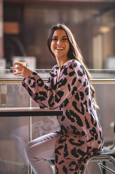 Urban chic: a happy latina model in a pink animal print sweater enjoying her coffee in the morning - Photo, Image