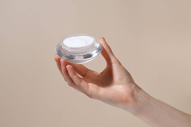 Female hand holding jar of facial moisturizer cream on beige isolated background. Treatment, spa, beauty, skincare cosmetic product - Foto, Imagem
