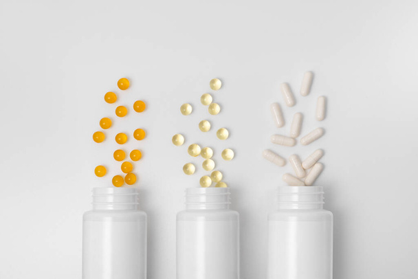 Three blank jars with yellow, orange and white capsules pills on a gray isolated background. Concept of health, medicines and pharmacy. Image for your design - Foto, Imagen