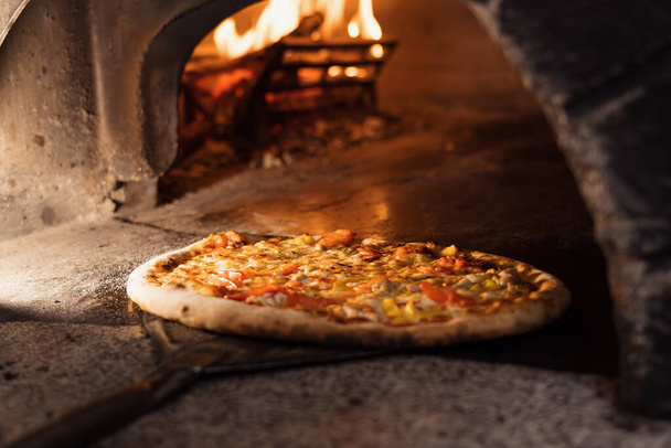 Pizza concept. Preparing traditional italian pizza. Long shovel for pizza, baking dough in a professional oven with open fire in interior of modern restaurant kitchen. High quality photo - Photo, Image