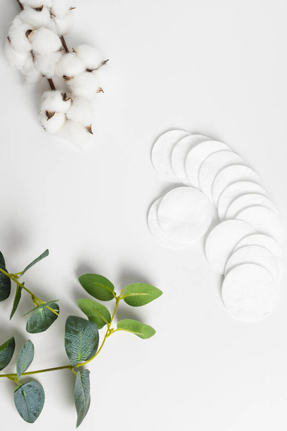 Almohadillas de algodón decoradas con hojas de plantas y flores de algodón sobre un fondo blanco. plano, vista superior, espacio para copiar. - Foto, Imagen
