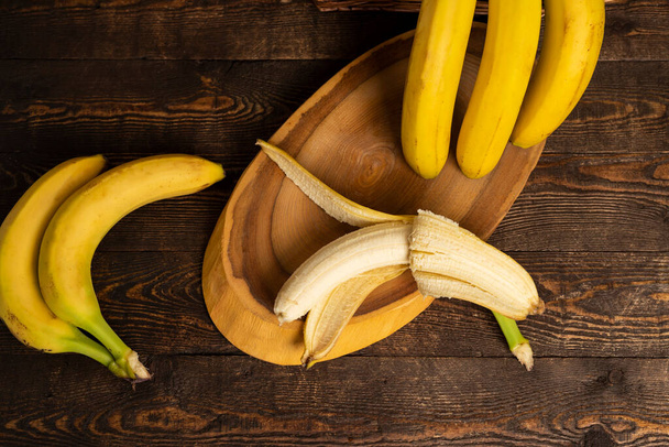 Bunch of bananas in a wicker basket and wood slicing board against a wooden background. top view, flat lay, copy space. - Photo, Image