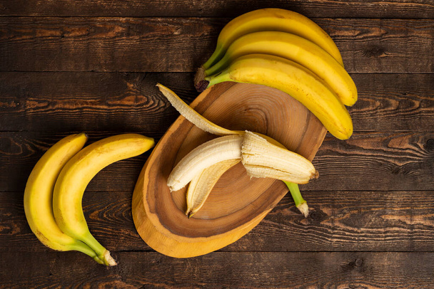 Bouquet de bananes dans un panier en osier et planche à trancher sur un fond en bois. vue du dessus, plan, espace de copie. - Photo, image