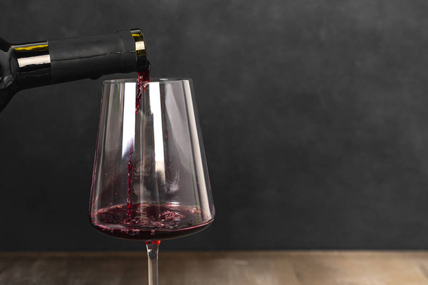Víno se nalévá do sklenice na tmavě šedém nebo černém pozadí. - Fotografie, Obrázek