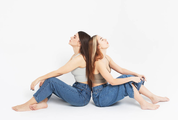 lifestyle, fashion and people concept: Two young female friends sitting on the floor together. - Foto, imagen