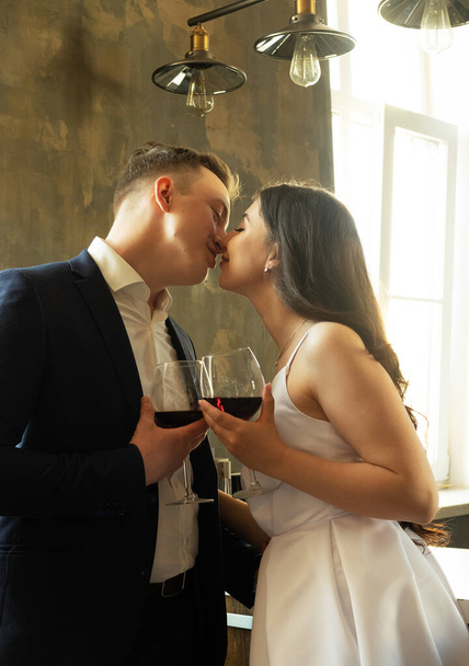 Family and young people concept: Young newlywed couple drinking wine and smiling at their happiness, romance and tenderness - Foto, Bild