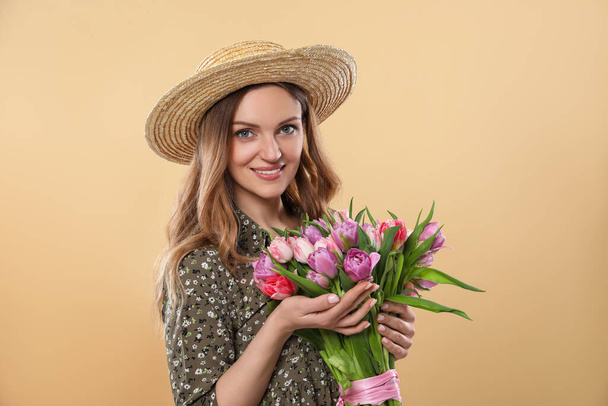 Happy young woman in straw hat holding bouquet of beautiful tulips on beige background - Foto, Imagem