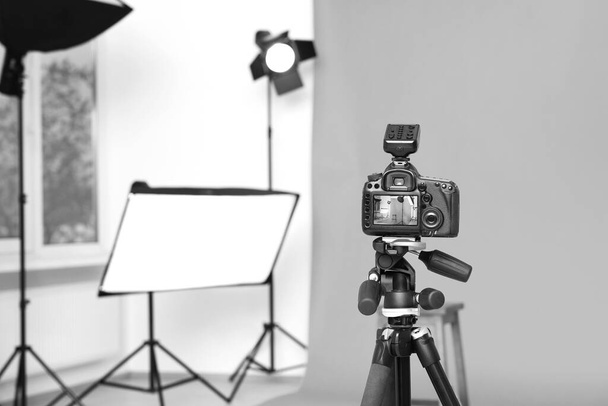 Camera on tripod, bar stool and professional lighting equipment in modern photo studio, space for text - Foto, afbeelding