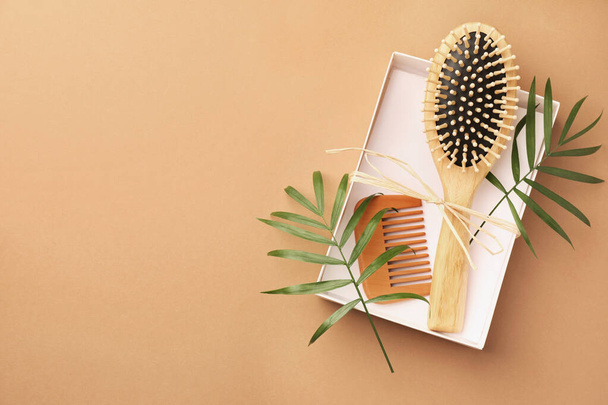 Wooden hairbrush, comb and green leaves on light brown background, top view. Space for text - Фото, изображение