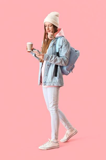 Female student with cup of coffee using mobile phone on pink background - Zdjęcie, obraz