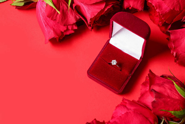 Κουτί με δαχτυλίδι αρραβώνων και τριαντάφυλλα σε κόκκινο φόντο - Φωτογραφία, εικόνα