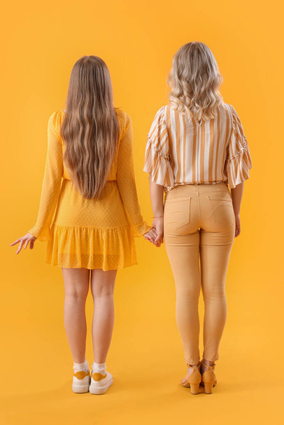 Hermanas jóvenes cogidas de la mano sobre fondo amarillo, vista trasera - Foto, imagen