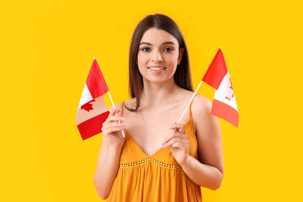 Young woman with flags of Canada on yellow background - 写真・画像