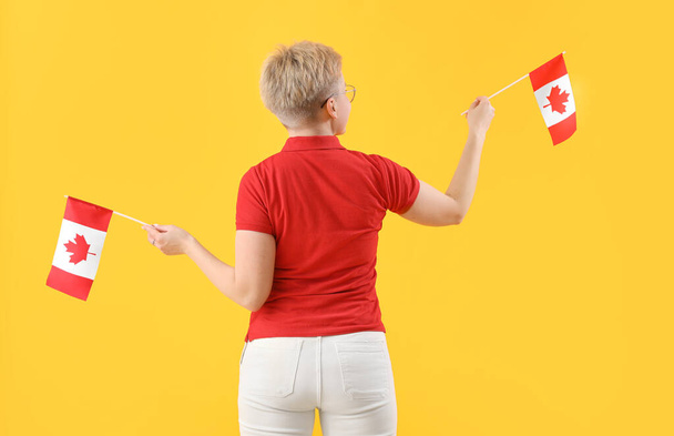 Jonge vrouw met vlaggen van Canada op gele achtergrond, achteraanzicht - Foto, afbeelding