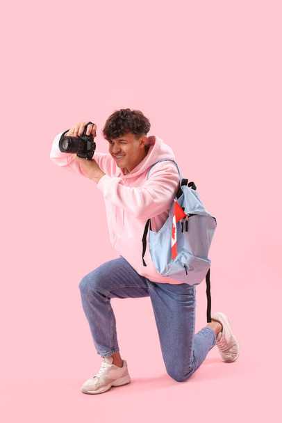 Fiatal férfi fényképezőgéppel, hátizsák és zászló Kanada rózsaszín háttér - Fotó, kép