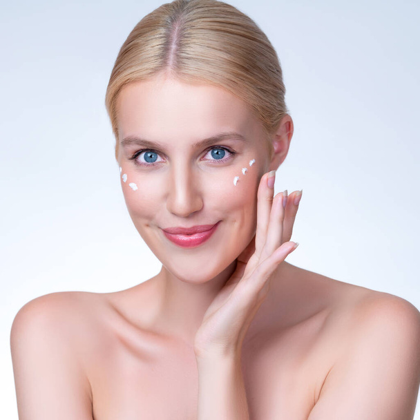 Personable beautiful perfect clean skin soft makeup woman finger applying moisturizer cream on her face under contour eye for anti aging wrinkle. Facial skin rejuvenation in isolated background. - Photo, Image