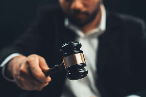 Focus wooden gavel hammer with burred lawyer in black suit holding gavel in background on his desk, symbol of legal justice and integrity, balanced and ethical decision in court of law equility - Foto, afbeelding