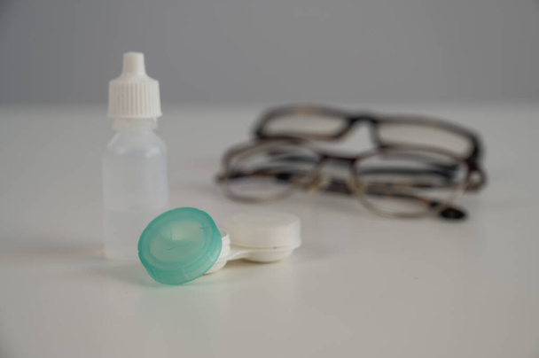 Two pairs of glasses lenses and contact drops in the eyes on a white table - Φωτογραφία, εικόνα