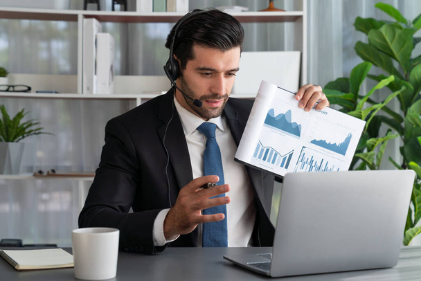 Business man wearing headphone present financial data or BI paper via laptop during online meeting. Remote work concept with virtual meeting presentation of effectiveness remote work. Fervent - Фото, зображення