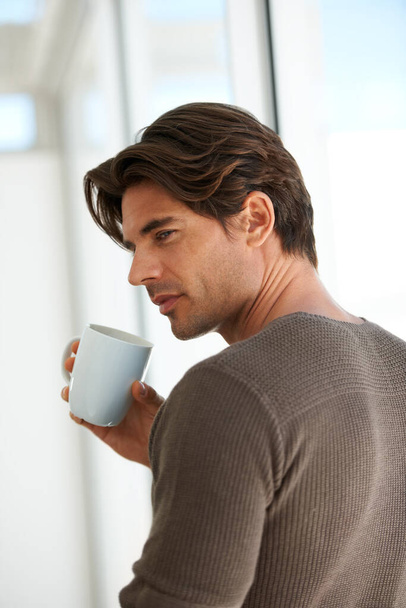 Esperando a que empiece la cafeína. Un joven guapo parado en casa y sosteniendo una taza de café - Foto, imagen