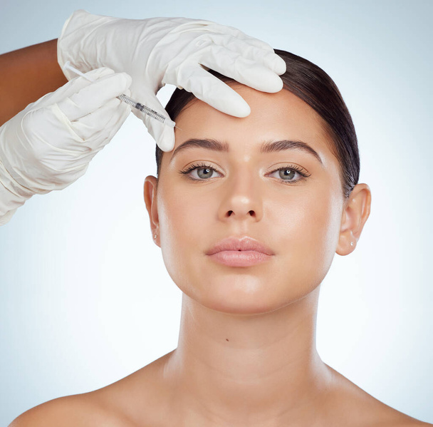 Closeup portrait of woman getting facial fillers or botox. Young caucasian model isolated against a grey studio background with copyspace. Dermatologist injecting patient during cosmetic procedure. - Fotoğraf, Görsel