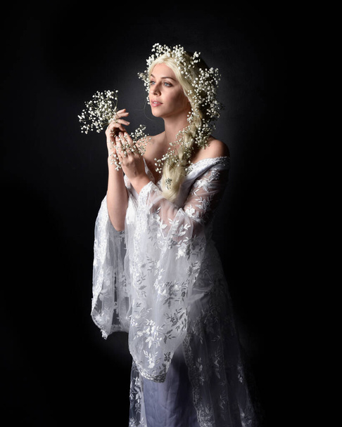 Close-up portret van mooie vrouwen met lang blond haar, het dragen van witte fantasie prinses bal jurk, houden mooie baby adem bloemen, geïsoleerd op zwarte studio achtergrond - Foto, afbeelding