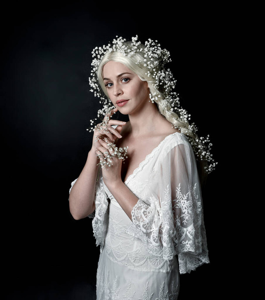 Close-up portret van mooie vrouwen met lang blond haar, het dragen van witte fantasie prinses bal jurk, houden mooie baby adem bloemen, geïsoleerd op zwarte studio achtergrond - Foto, afbeelding